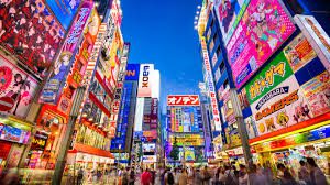 Asian Shares Mixed Amid Nvidia Boost and Wall Street Retreat Brightly lit street in Tokyo bustling with people and adorned with vibrant billboards and signs, showcasing the lively atmosphere of the city's commercial area.